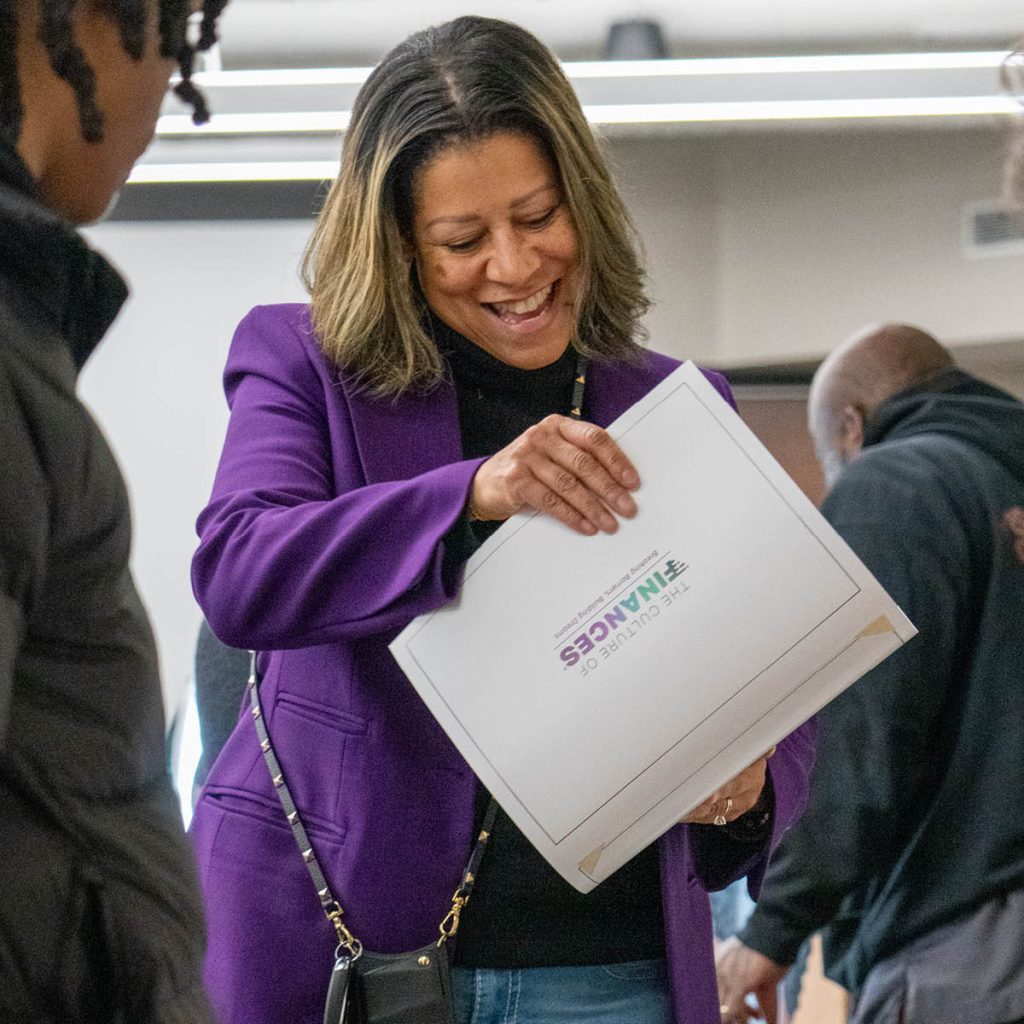 A person wearing a purple jacket, smiles big while looking at the Culture of Finances completion certificate.