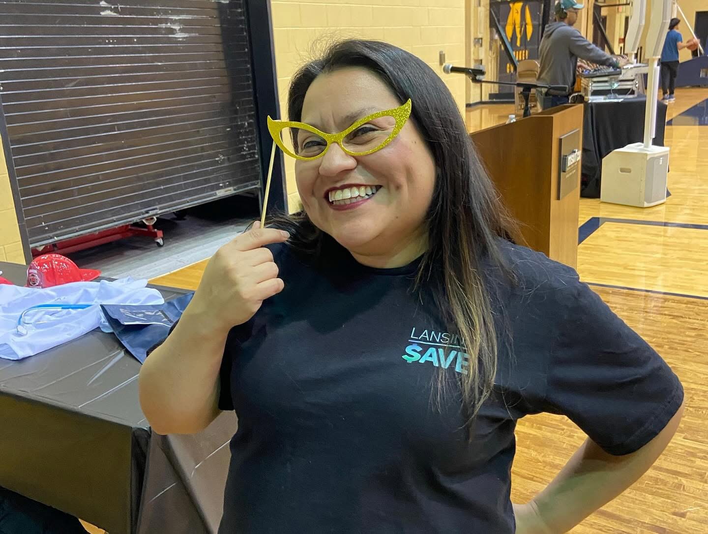 Lansing SAVE's Miss Cece smiles big while holding photo prop glasses