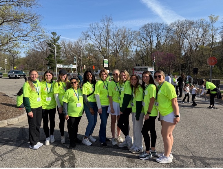 A group of MSUFCU employees in lime green tshirts stand together on a sunny day.