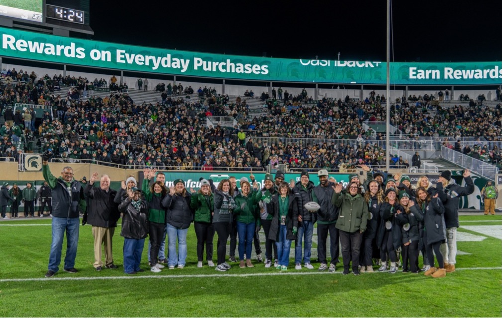 A group of people representing MSUFCU and MSU Athletics standing of the MSU football field.