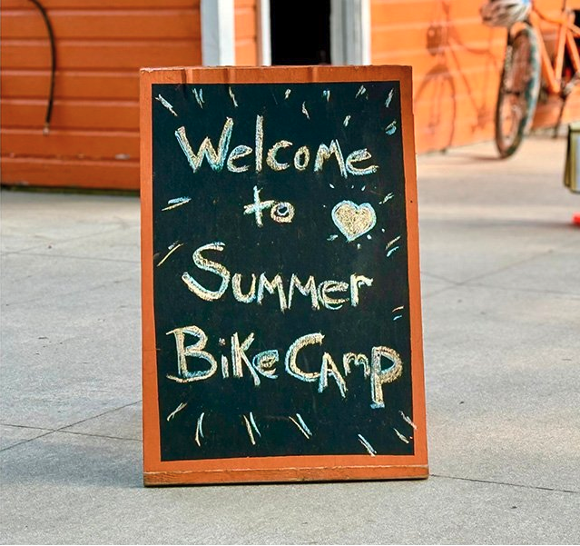 A chalk board sitting on the sidewalk reads "Welcome to Summer Bike Camp."